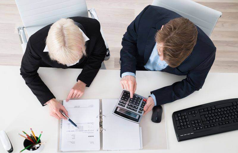 two men looking at accounting records and using a calculator to figure out profits and losses