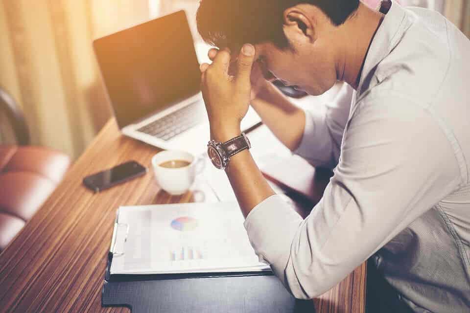 Individual Business owner struggling over clipboard and computer with coffee cup and phone sitting at a desk finance and accounting frustrations can be handled by ATS Accounting and Tax Edmonton